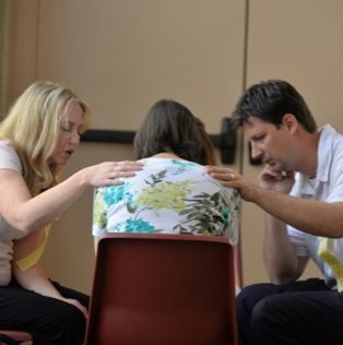 A man and two women are sitting in a circle with their hands on each other 's shoulders.