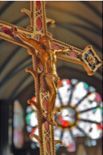 A cross with jesus on it in a church with a stained glass window in the background.