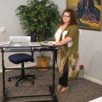 A woman is standing at a standing desk in a room.