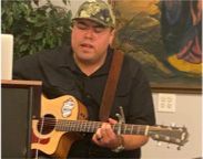 A man is playing an acoustic guitar in front of a painting.