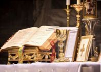 A bible is sitting on top of a table next to a chalice and candles.