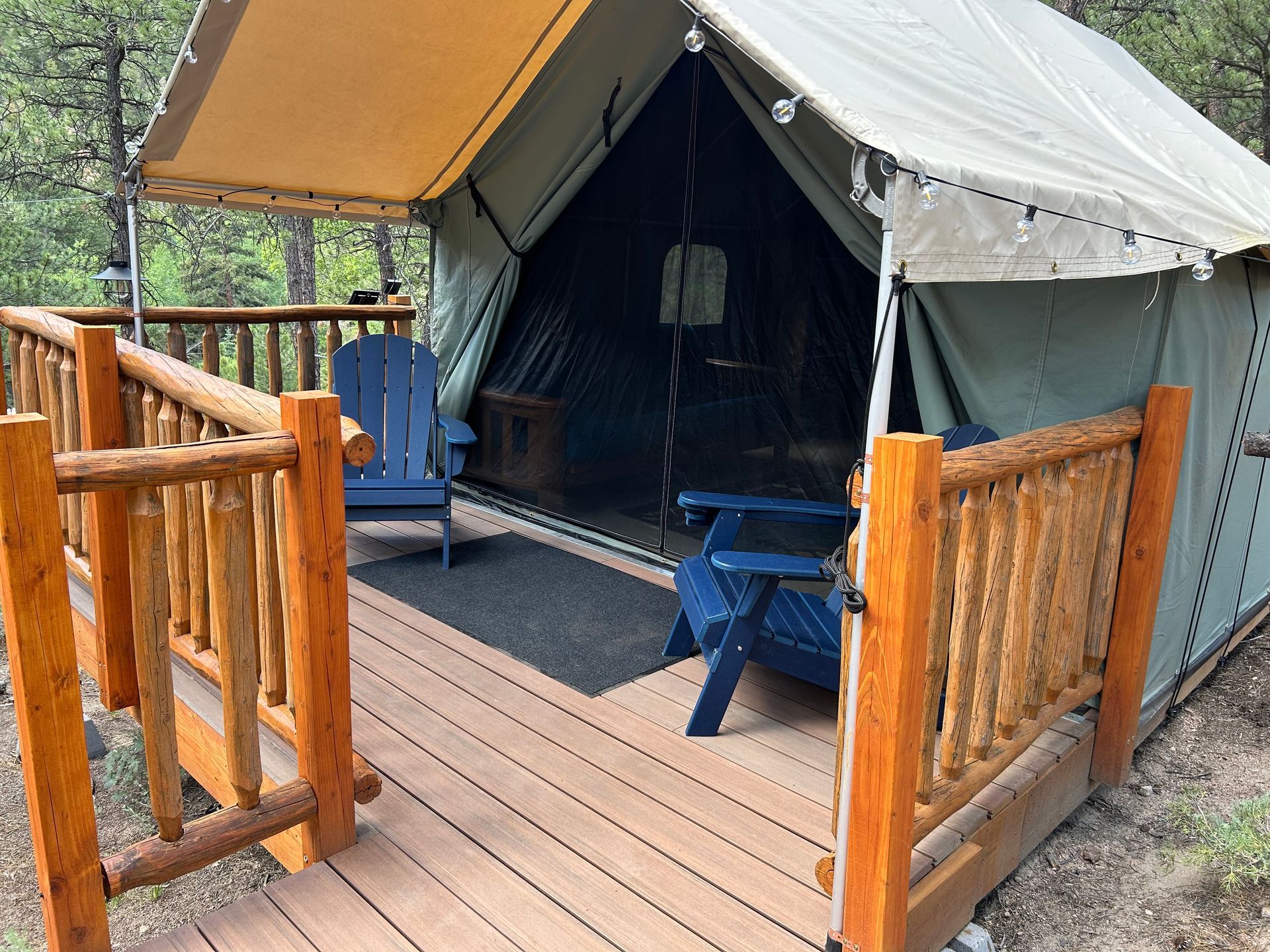 Canvas tent on a wooden deck with two blue chairs. The tent has a canopy and string lights.