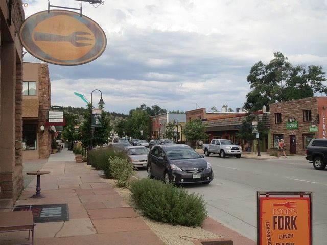 Street view with a fork sign, shops, cars, and a cloudy sky.