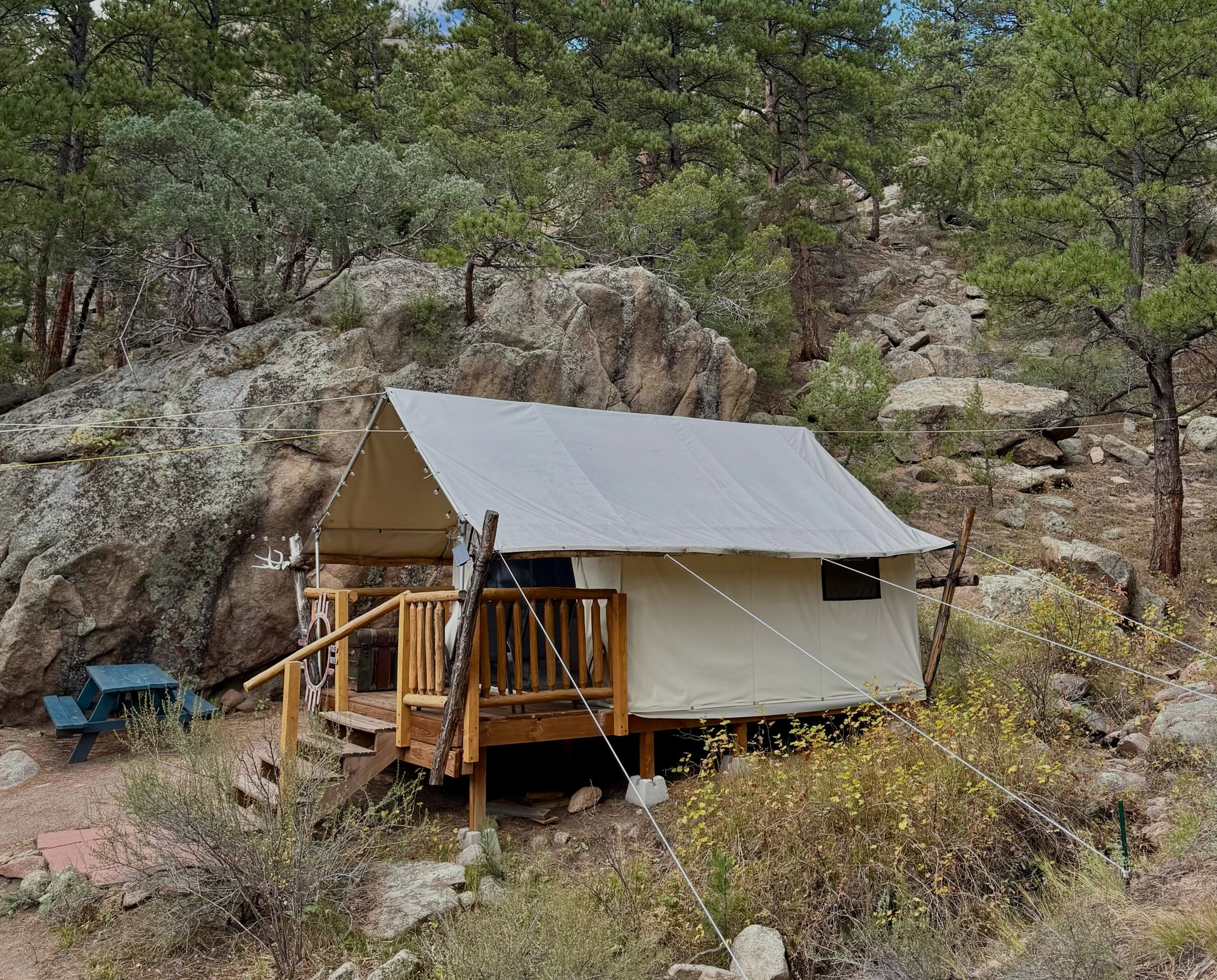 Tan canvas tent on a wooden deck in a rocky, wooded area.