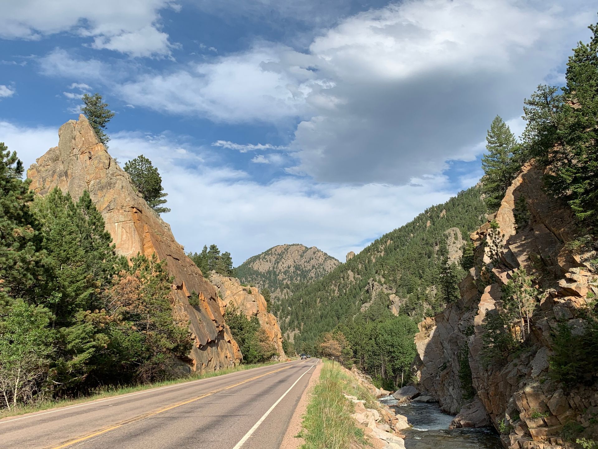 Road through a rocky mountain pass, blue sky with clouds, trees on the slopes.