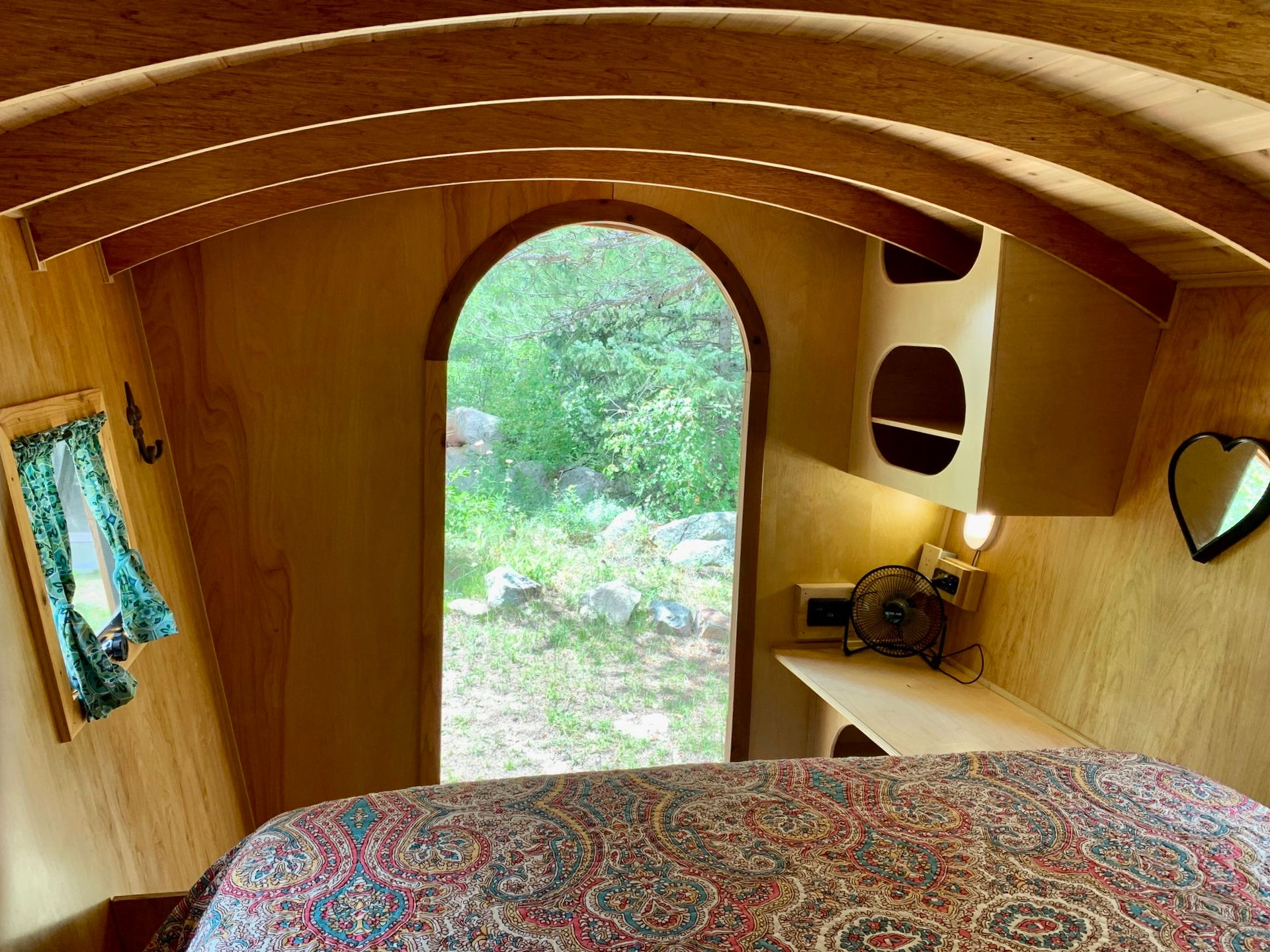 Cozy interior of a wooden structure with arched doorway, bed, and built-in shelves.