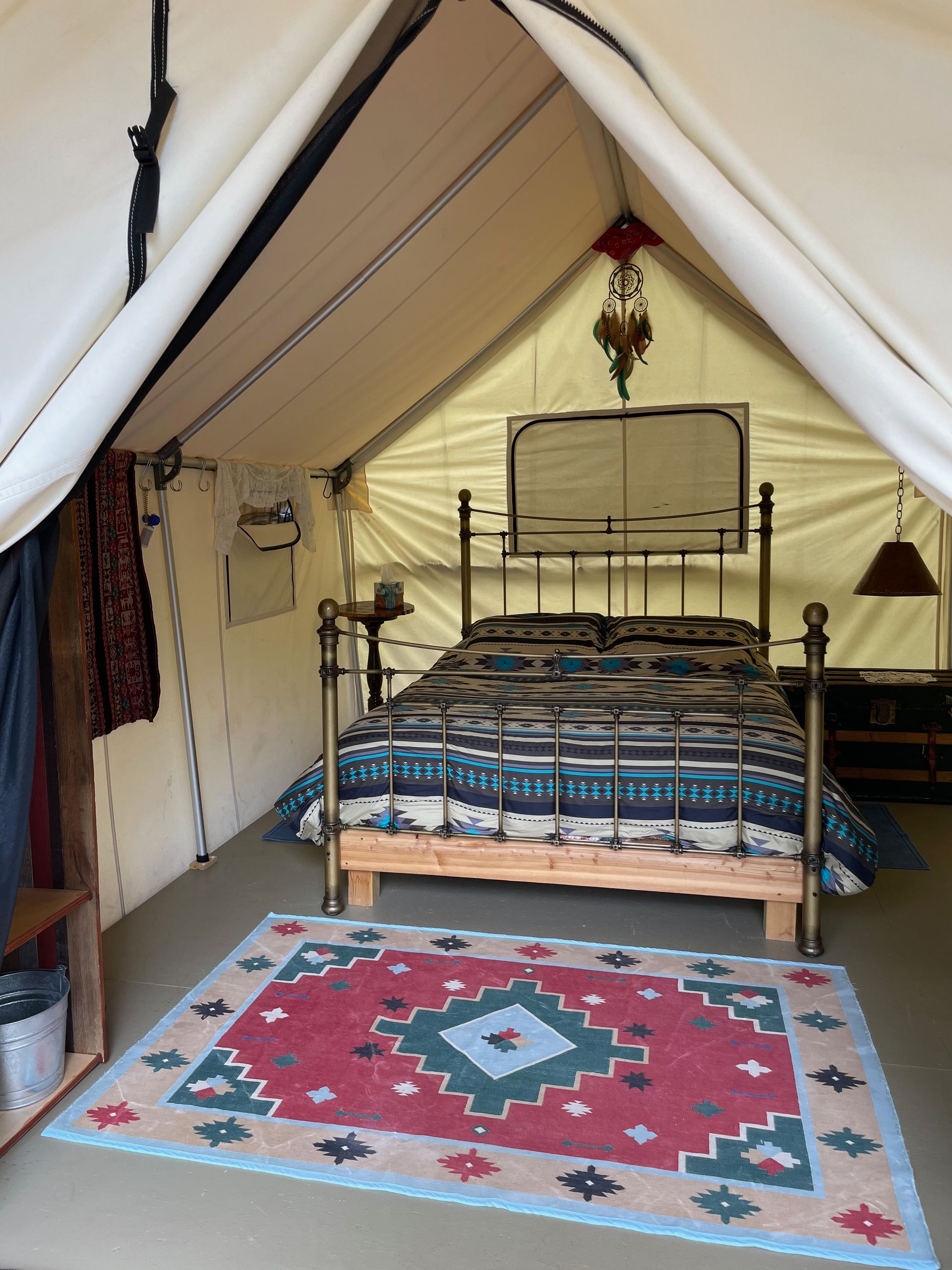 Inside of a canvas tent with a bed, rug, and decorative hanging.