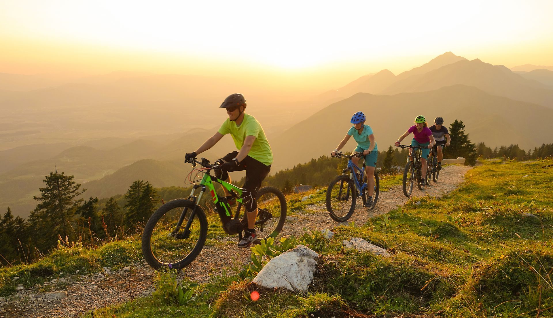 People riding mountain bikes on a trail in the mountains at sunset.