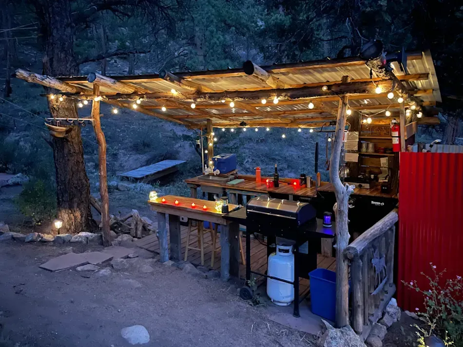 Outdoor rustic kitchen with a grill, lights, and a wooden canopy.