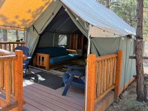 Canvas tent on wooden deck with furniture inside, in a wooded area.