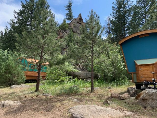 Campground scene: teal-roofed cabins nestled in a wooded area with rocky hillside and two young pine trees.
