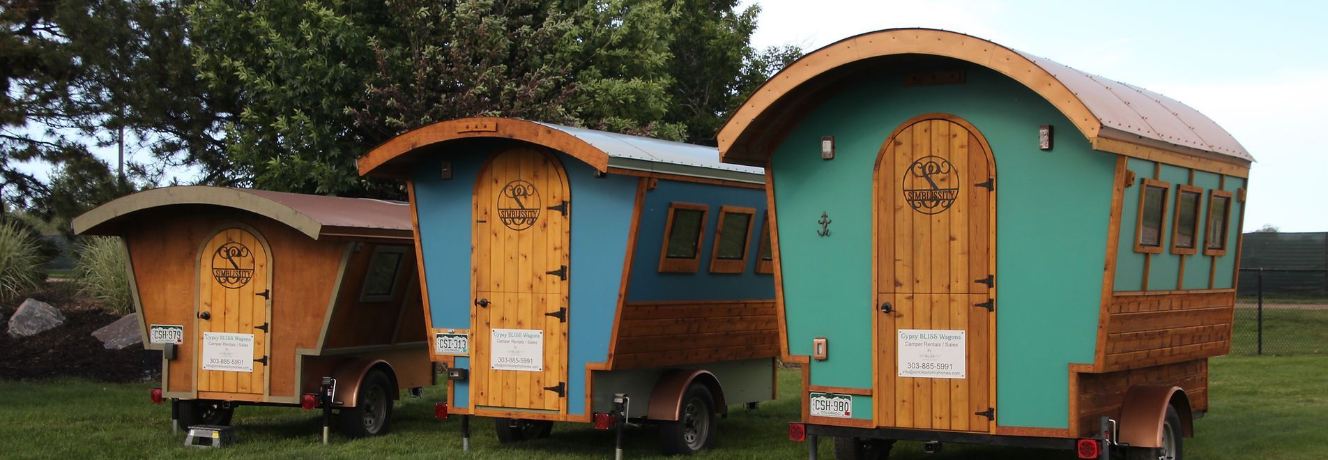 Three colorful, wooden wagons with rounded roofs are parked in a grassy area.