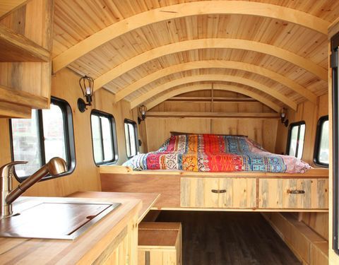 Wooden-paneled interior of a camper van with arched ceiling, bed, kitchen counter, and windows.