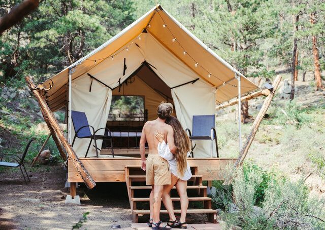 Couple embracing on deck of glamping tent in forest.