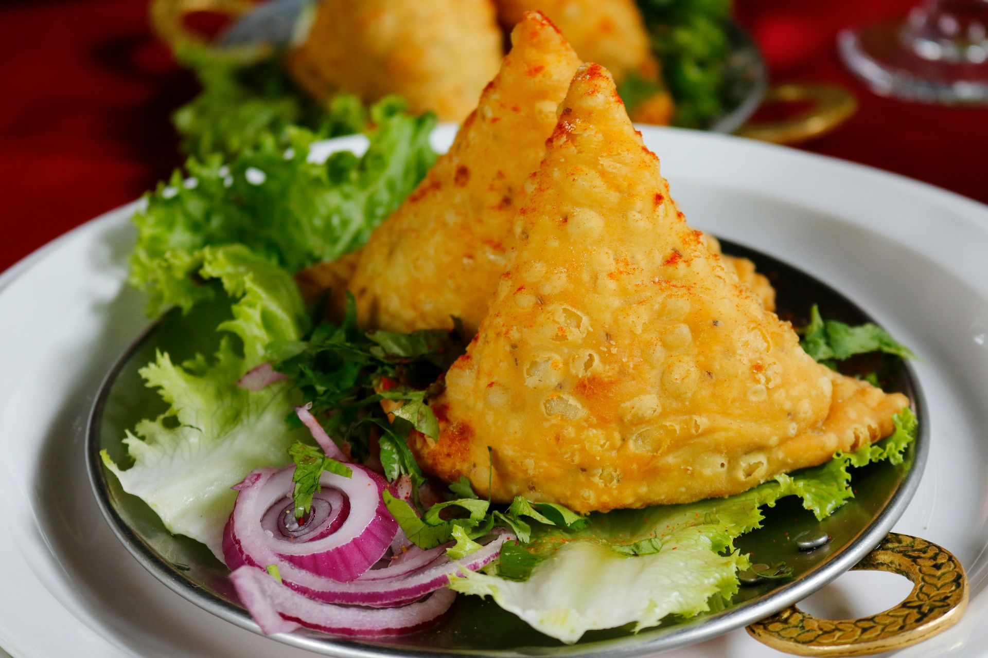 Two samosas on a bed of lettuce, with red onion.