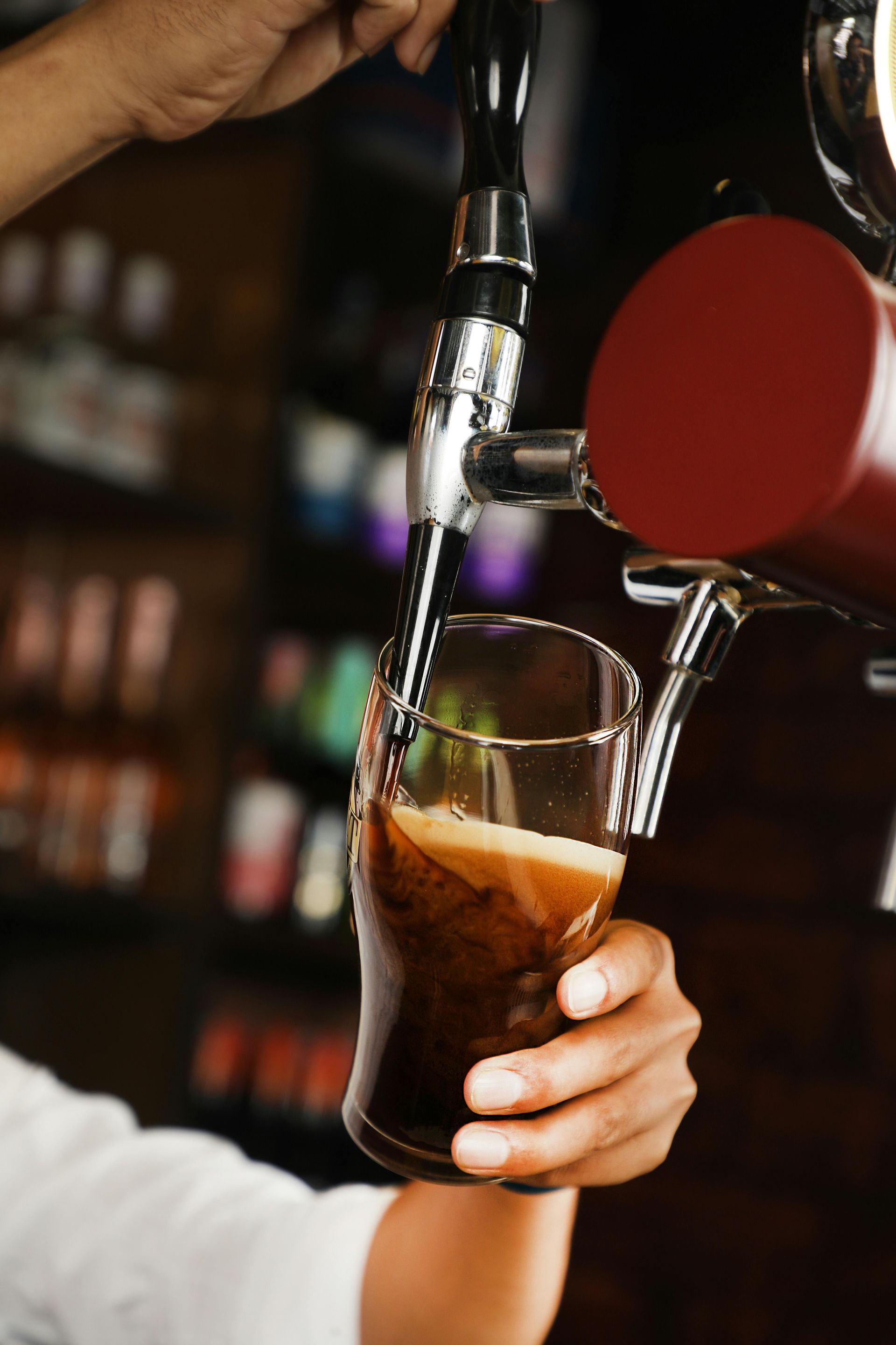 Hand pouring dark beer from a tap into a glass at a bar.