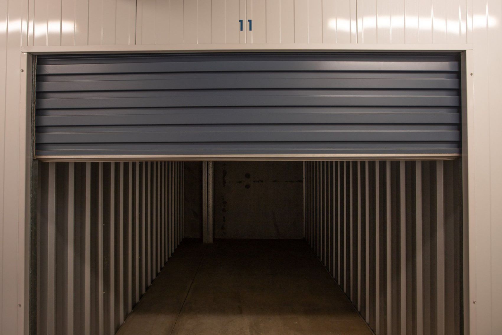 An Empty Storage Unit With a Roll Up Door Open — AKM Self Storage In Kurri Kurri, NSW