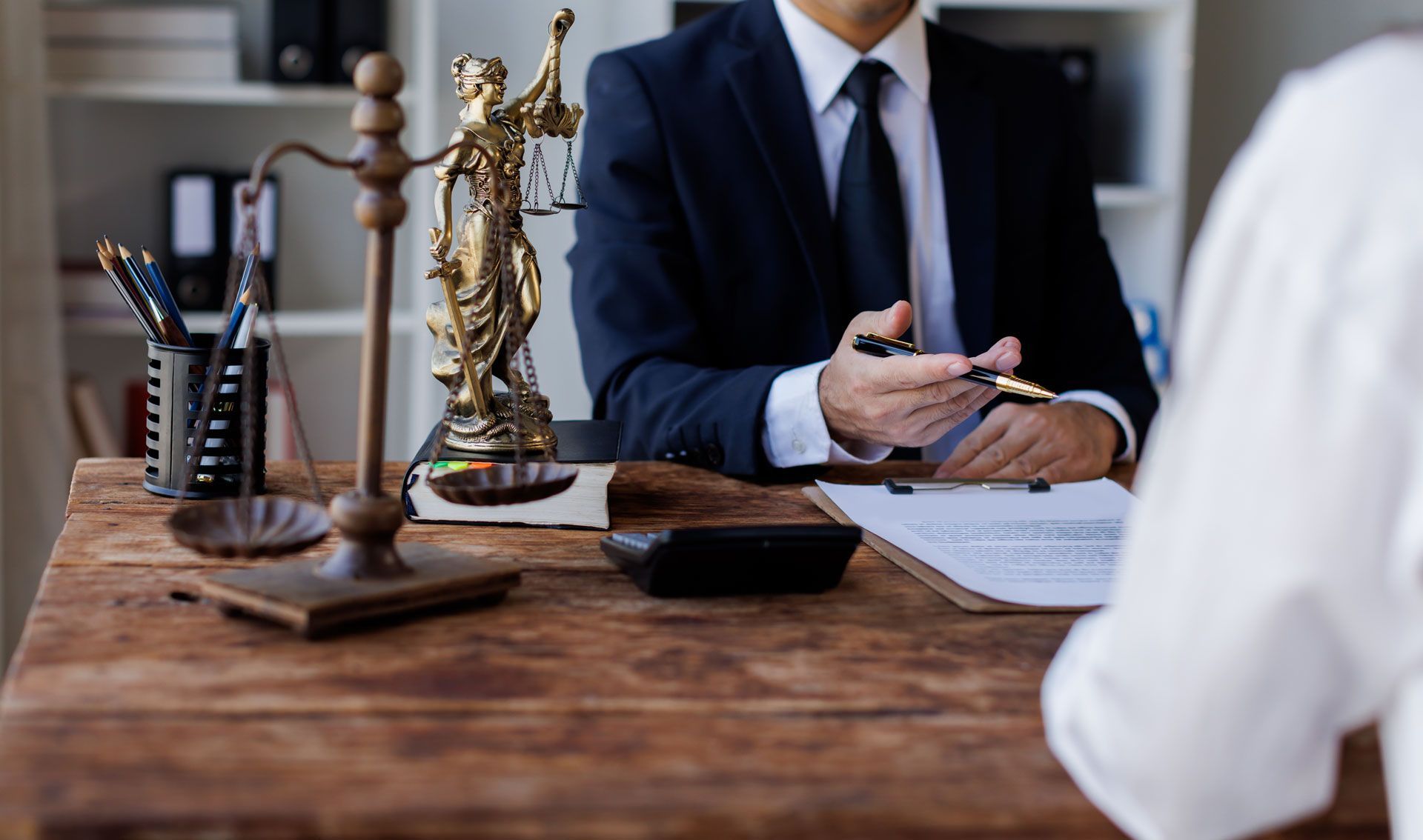 Lawyer in suit reviewing documents with client at a wooden desk, Scales of Justice on desk.