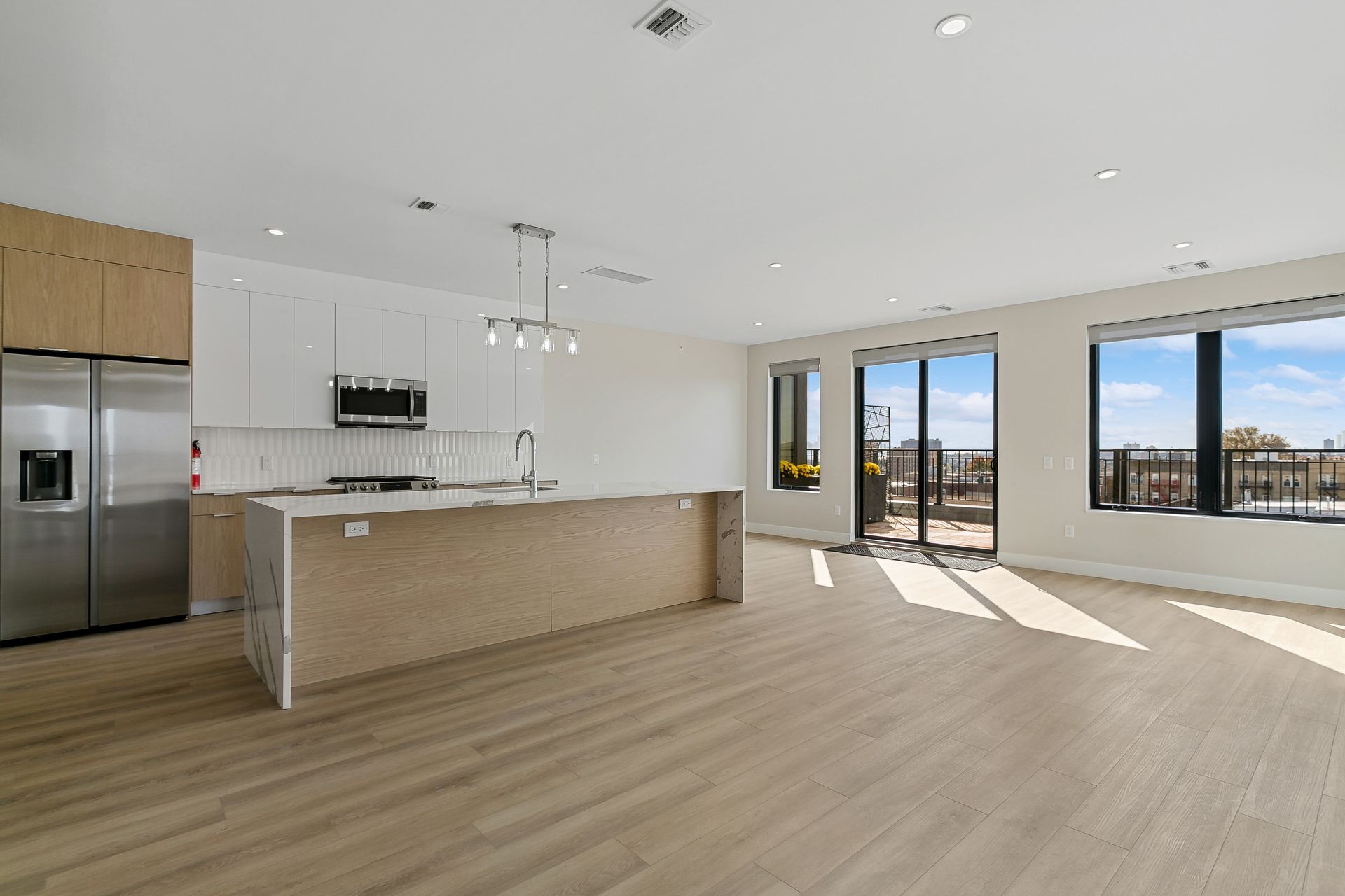 An empty kitchen with a large island and stainless steel appliances.