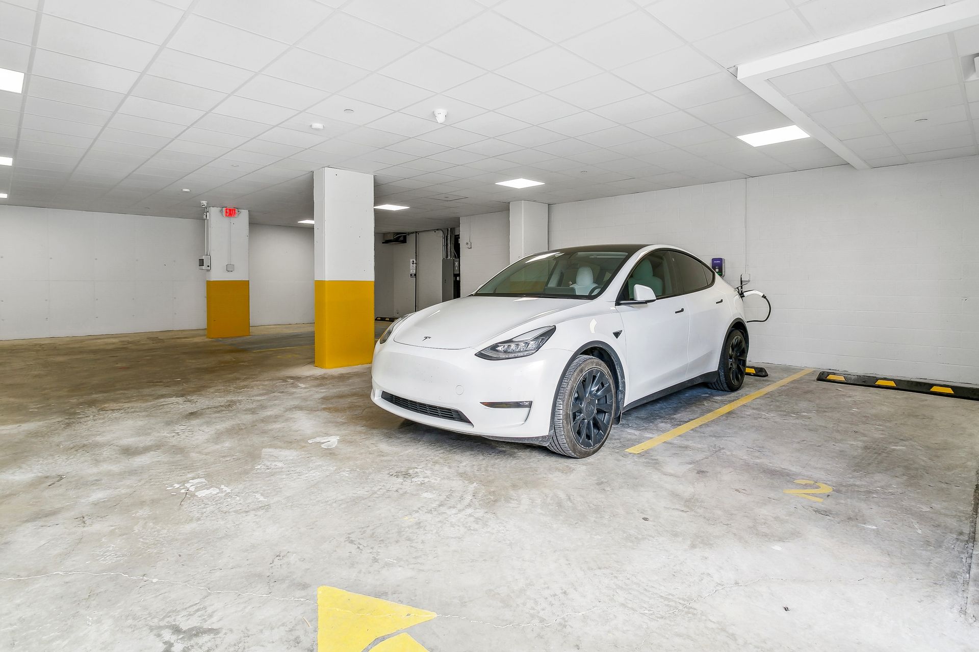 A white tesla model y is parked in a parking garage.