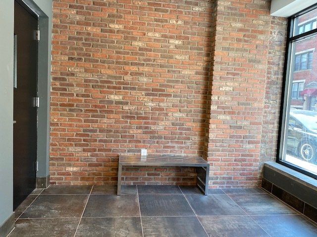 A room with a brick wall and a bench in front of a window.