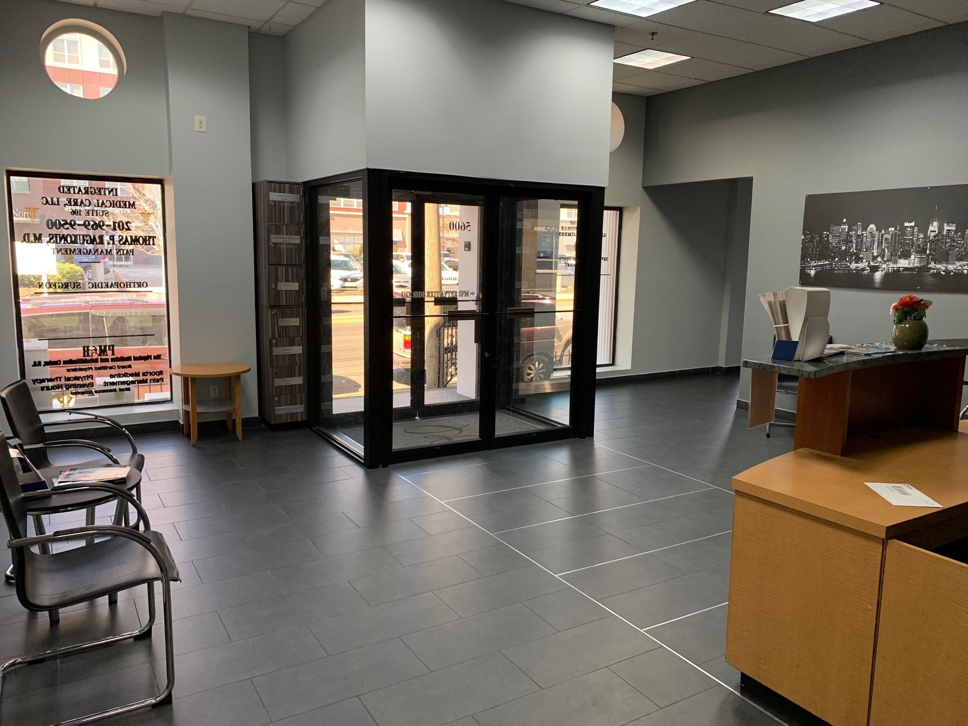 A waiting room with chairs , a desk , and a glass door.