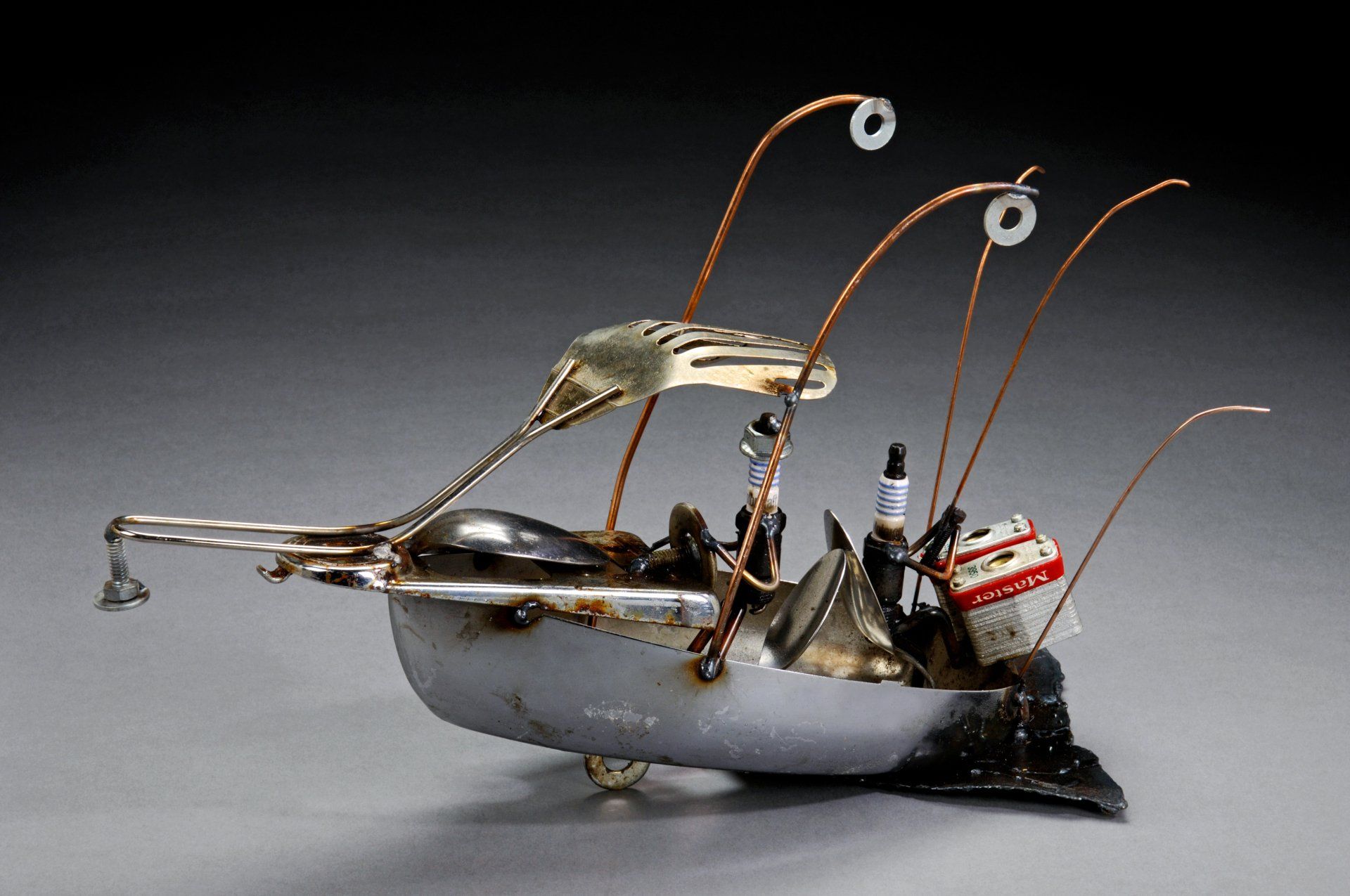 Sparkplug Sculpture of 2 Figurines in iron boat with padlock motor