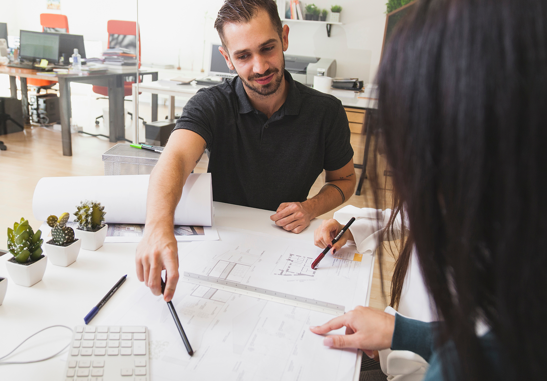Man and woman collaborating over blueprints in an office. Both point at the plans.