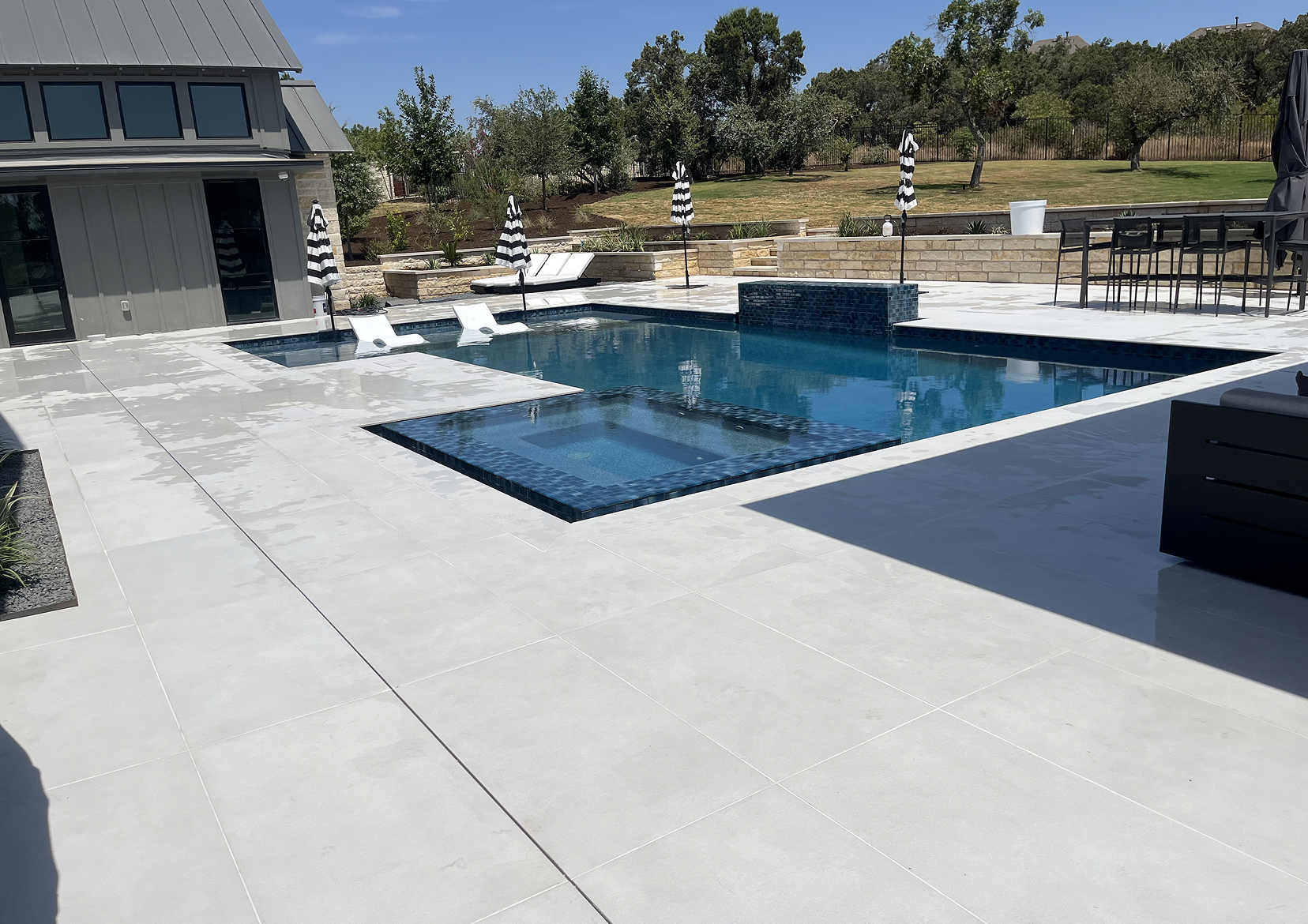 Pool area with a pool, patio, and modern house in background.
