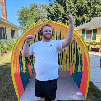 Man in front of a colorful tunnel, wearing headphones, raising an arm and posing outside.