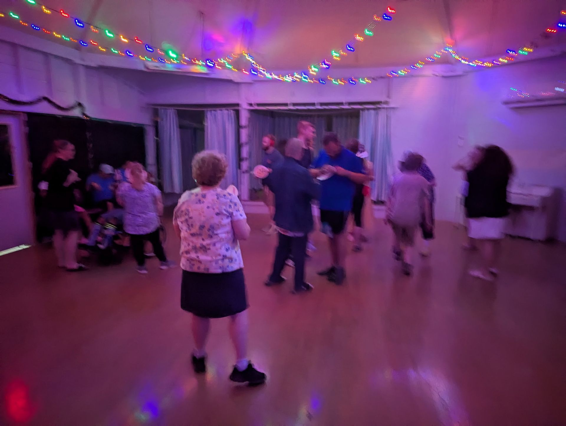 People dancing in a room decorated with fairy lights, with a wooden floor.