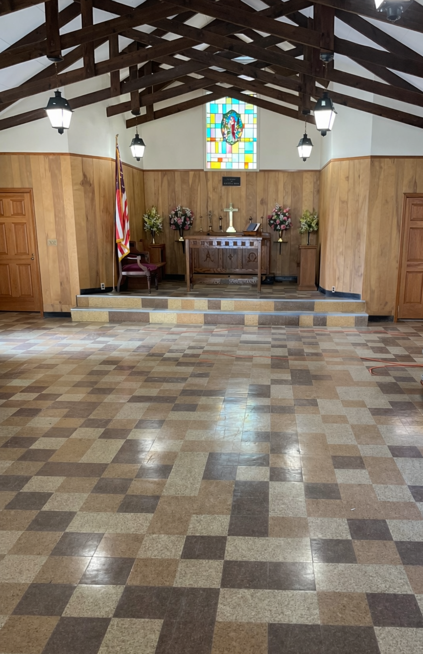 Empty church interior with wood paneling, checkered floor, and altar with stained glass window.