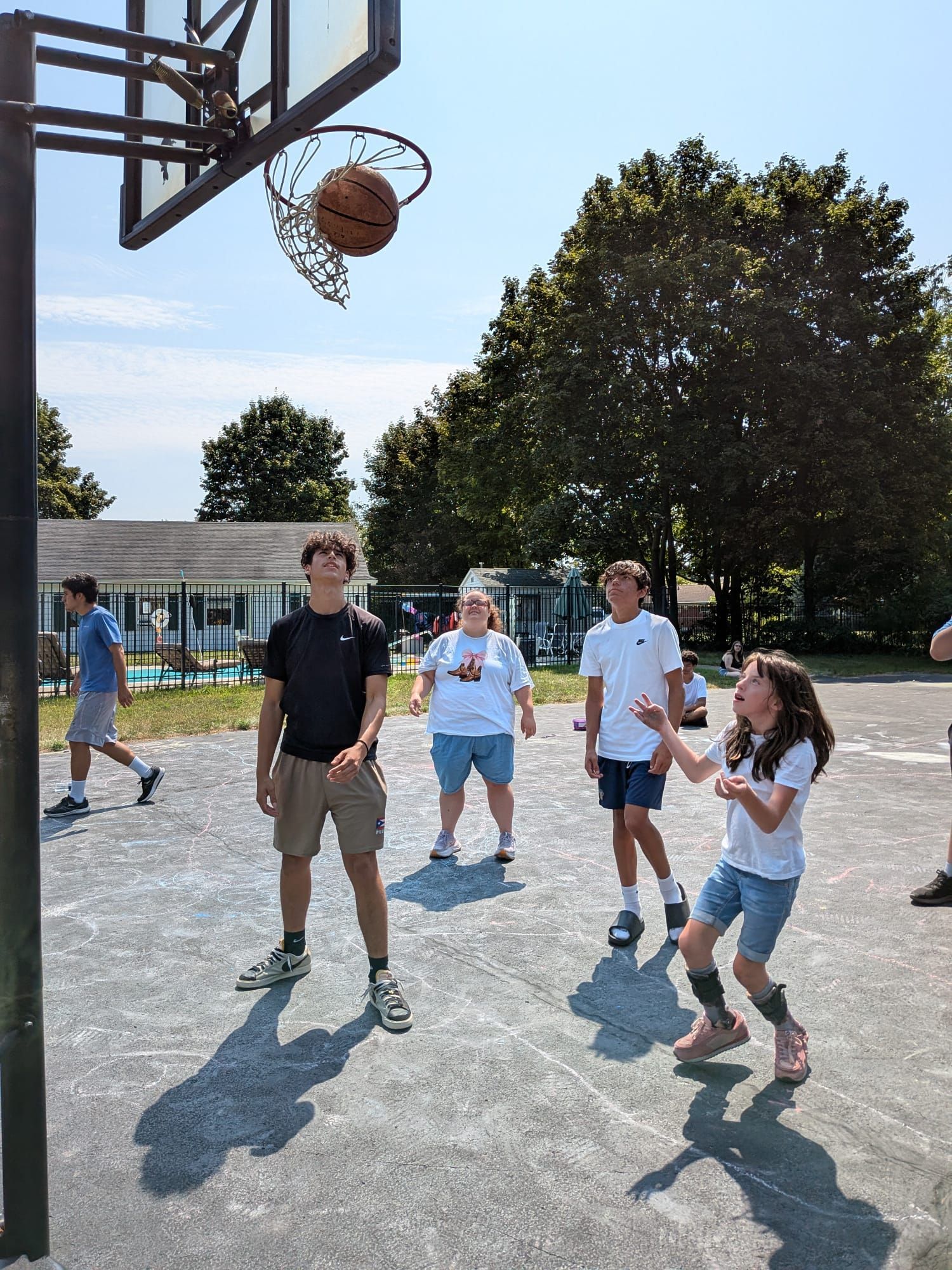 Group of teens working together on a rope bridge over a lake.
