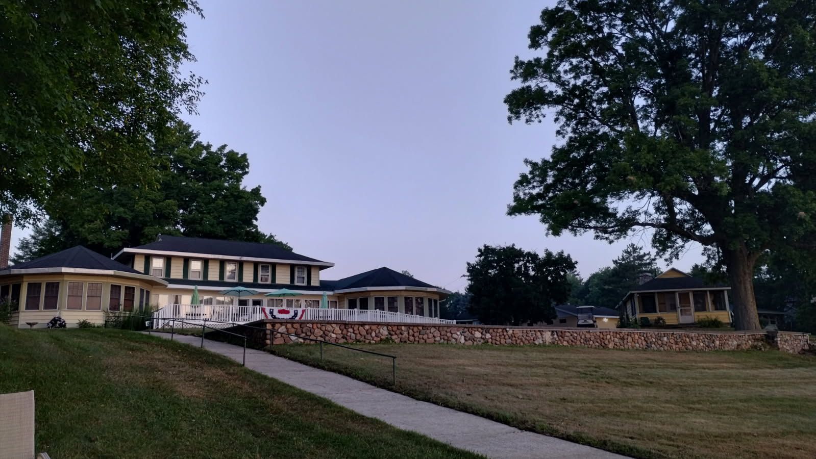 Large two-story house with stone wall and porch, set in grassy yard under a twilight sky.