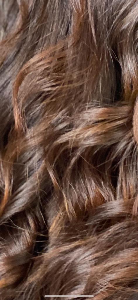 Primo piano di capelli ondulati, castano scuro, con riflessi castano più chiari.