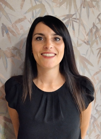 Donna sorridente con i capelli scuri, indossa un top nero e una collana d'argento.