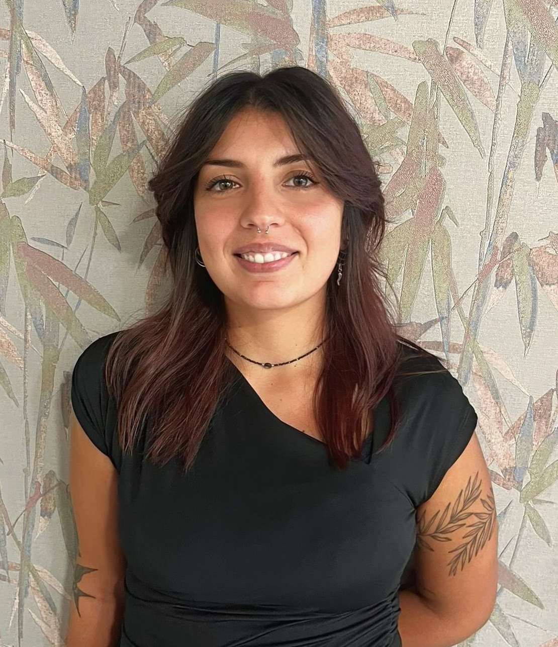 Una donna con un top nero sorride, in piedi davanti a una parete decorata.