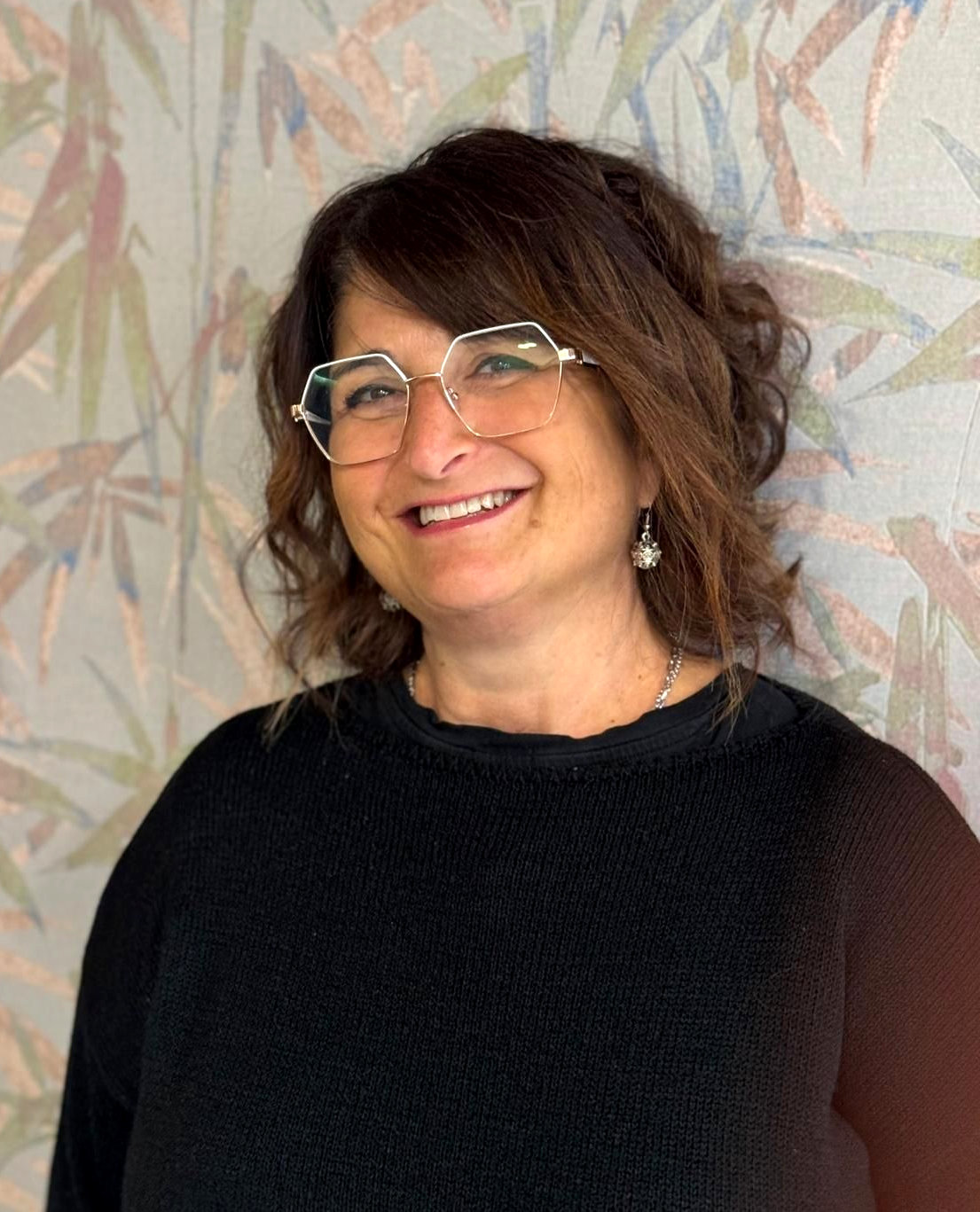 La donna con gli occhiali sorride, indossa una camicia nera e una collana.