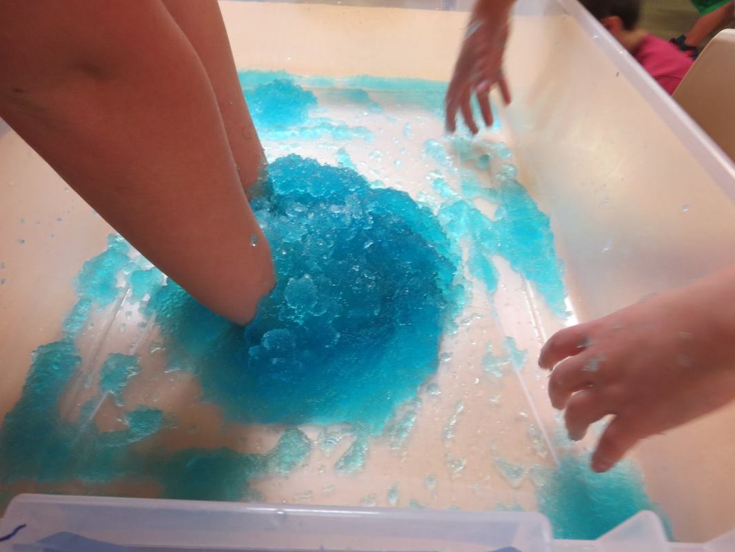 A child is playing with blue slime in a plastic container.