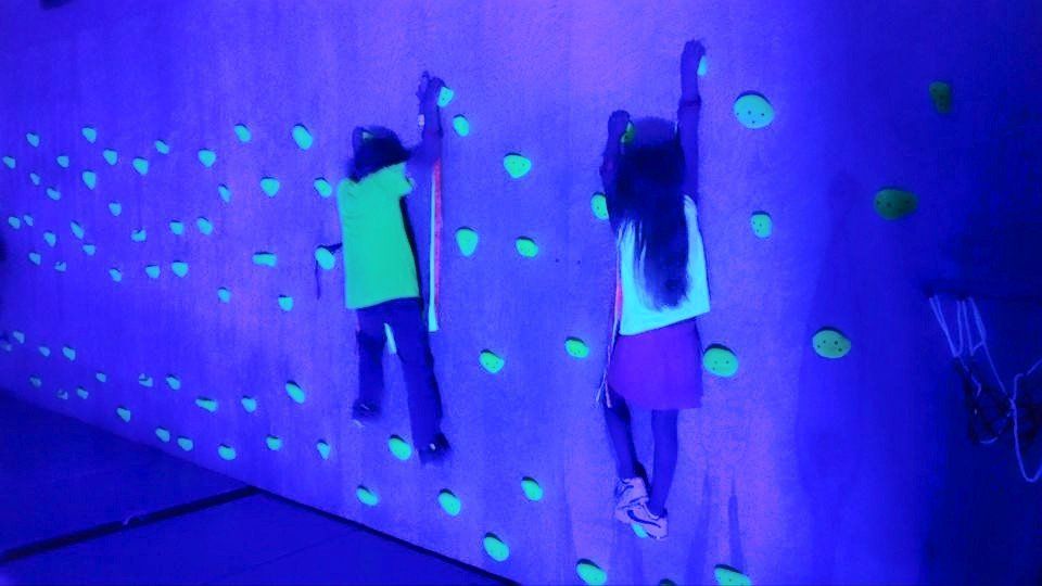 Two children are climbing a glow in the dark climbing wall.