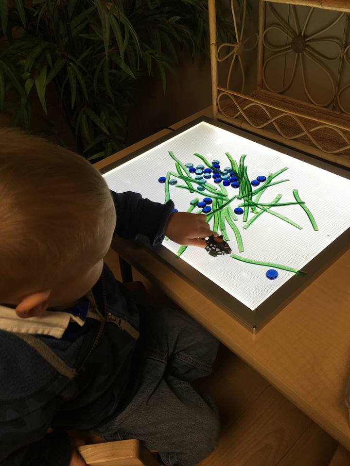 A young boy is sitting on the floor playing with a light box.
