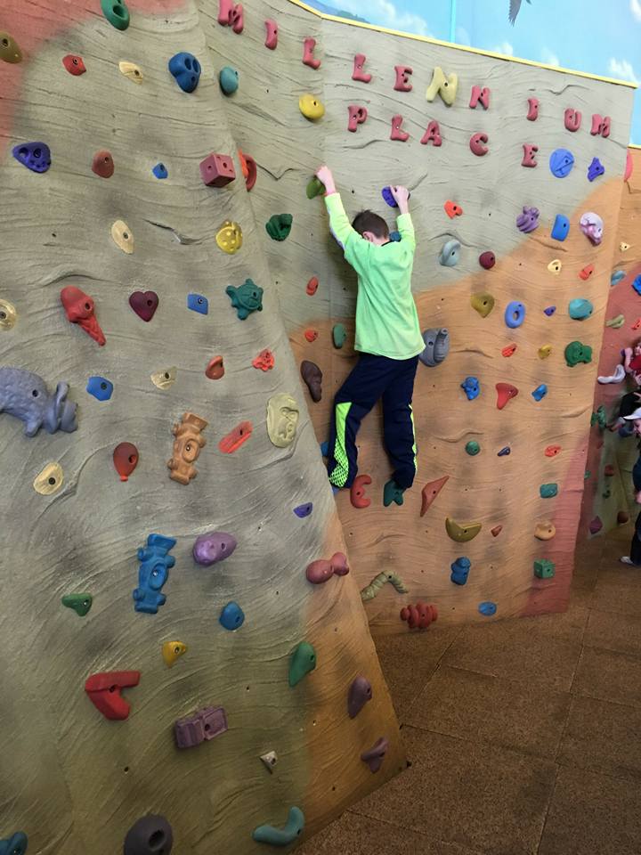 A boy in a green shirt is climbing a climbing wall