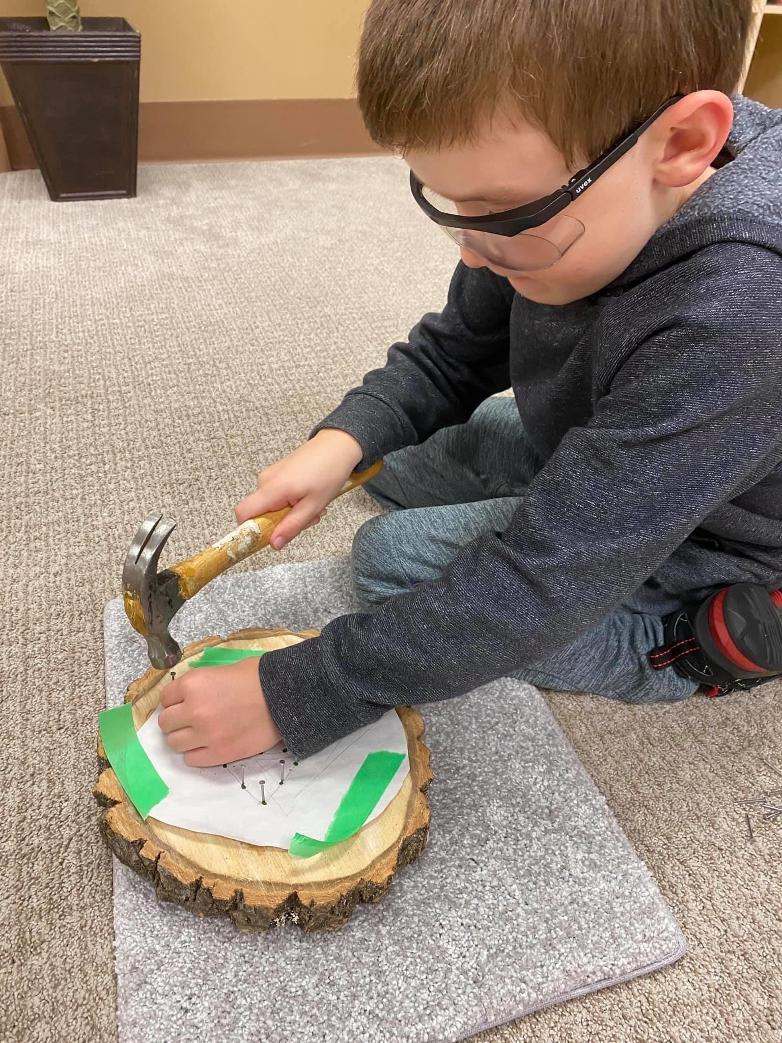 A young boy is hammering a nail into a piece of wood.