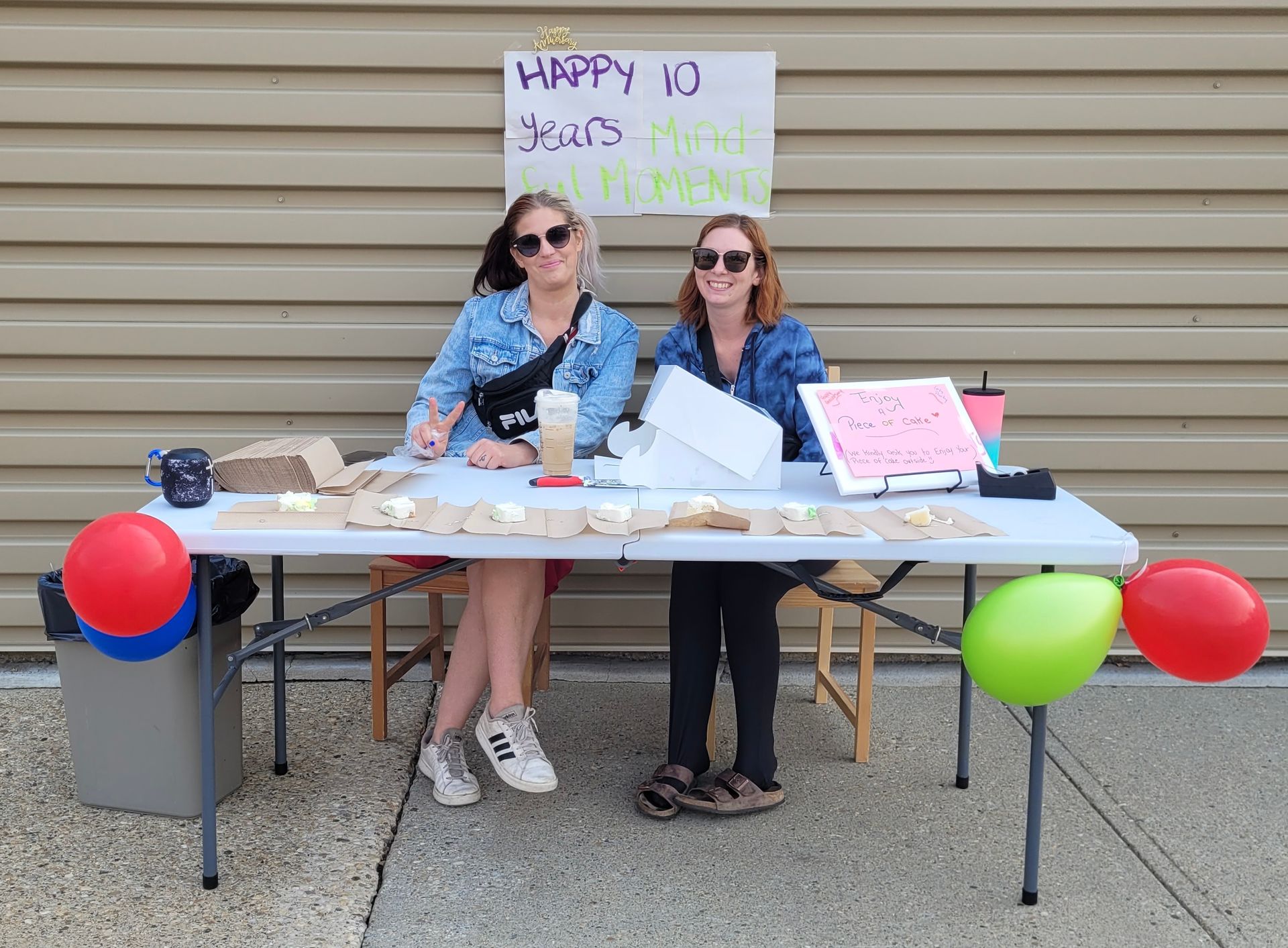 Two women are sitting at a table with balloons and a sign that says happy 10 years