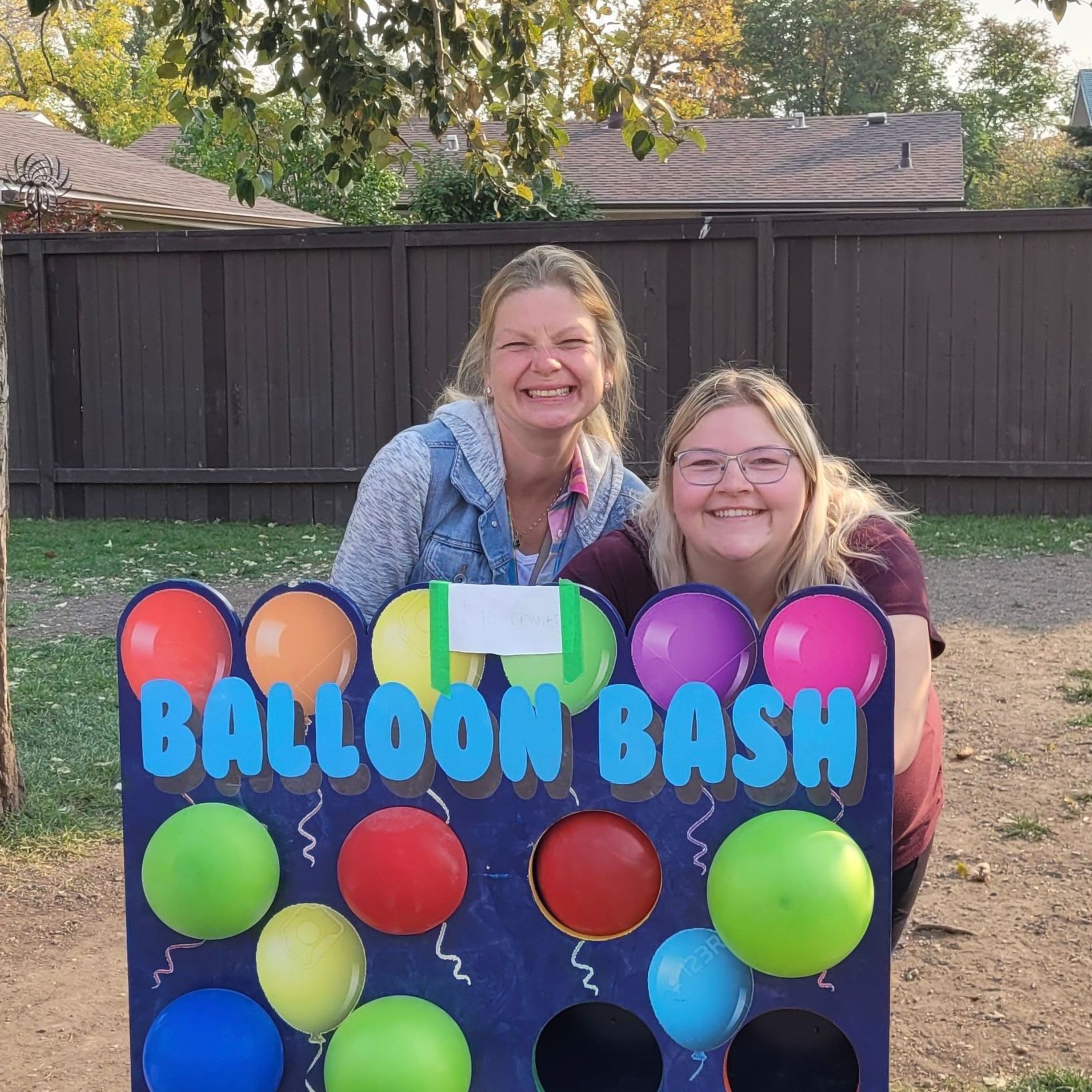 Two women are standing in front of a balloon bash sign