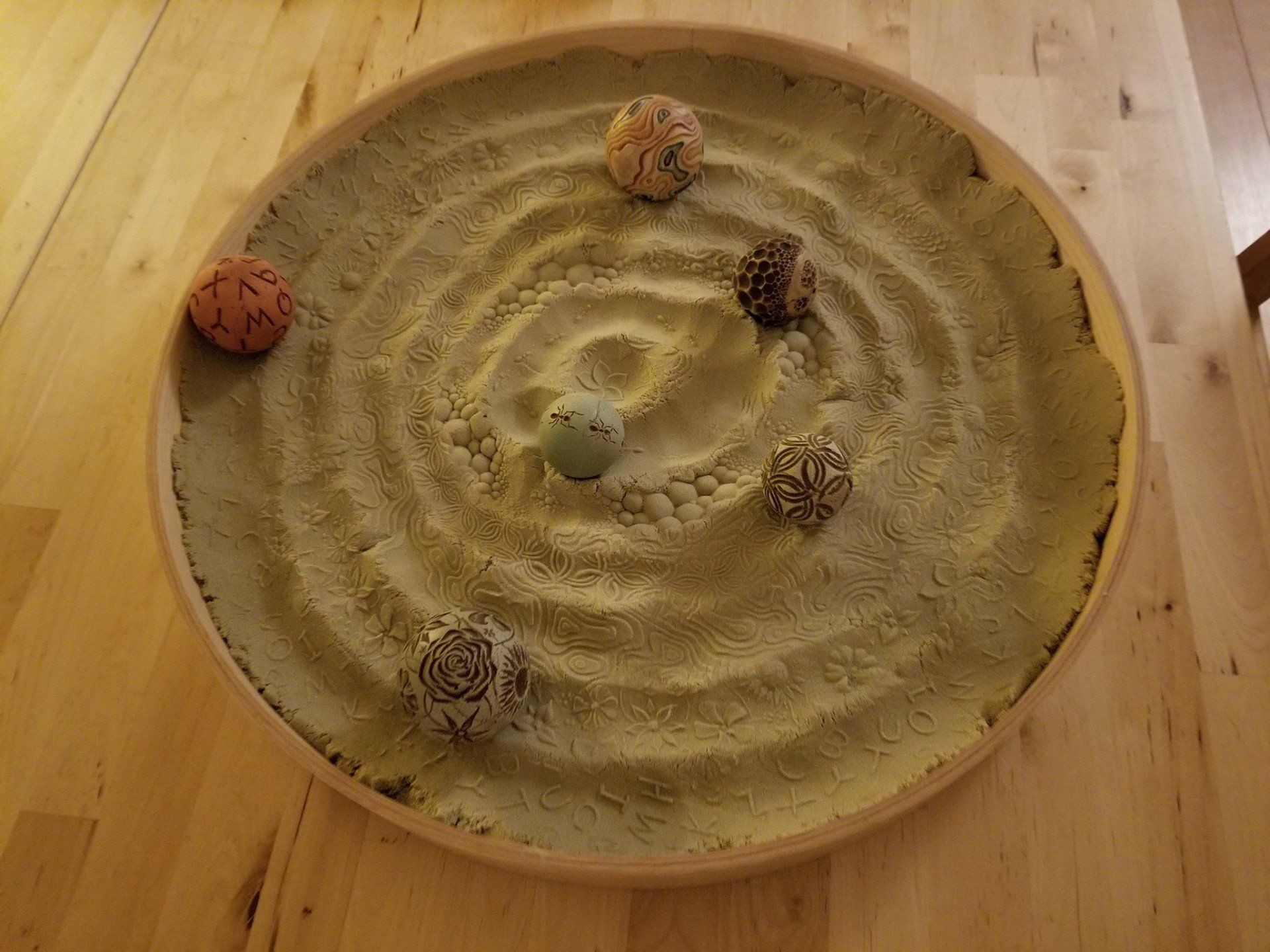 A wooden bowl filled with sand and rocks on a wooden table.