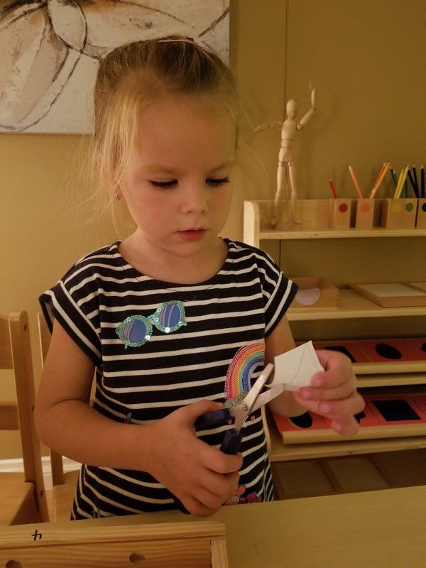 A little girl is cutting a piece of paper with scissors