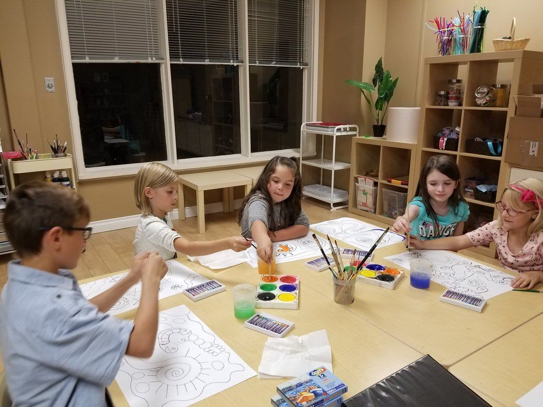 A group of children are sitting around a table painting with watercolors.