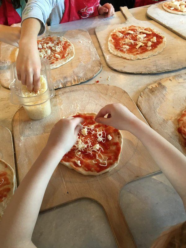 A group of children are making pizzas on wooden boards