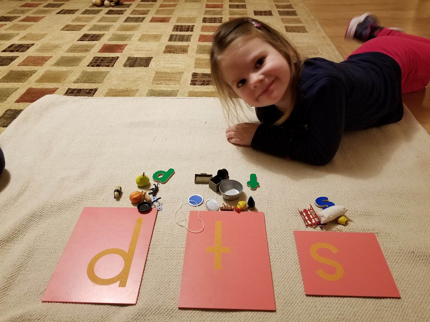 A little girl is laying on the floor playing with letters